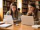 Une jeune étudiante compare deux ordinateurs portables fins sur une table de bibliothèque, entourés de cahiers et d’un chargeur USB-C.